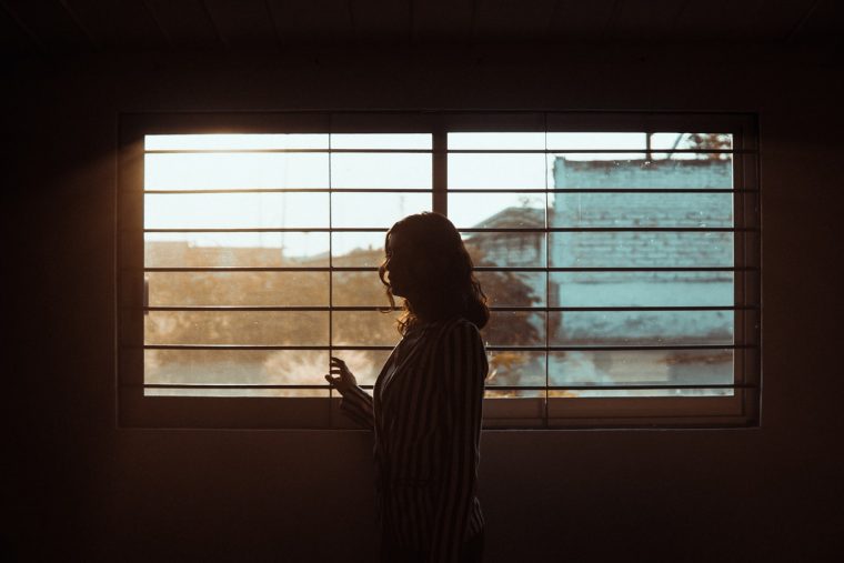 A woman looking out her window with sad lighting