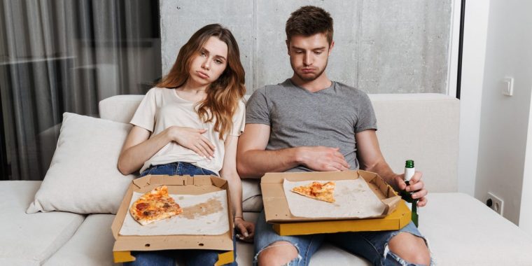 Man and woman feeling full after eating a pizza