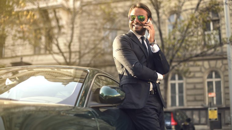 A rich looking guy leaning against an expensive car