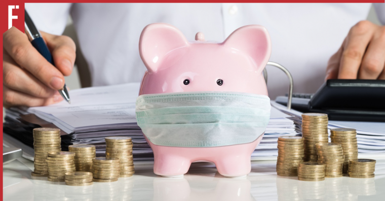 man counting money behind a piggy bank wearing a face mask