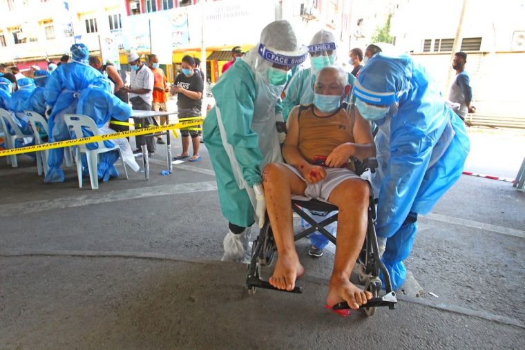 Malaysian front liners helping a senior person in a wheelchair