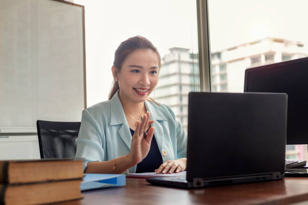 Beautiful female entrepreneur smiles as she participates in a web conference with colleagues. She is using a laptop.