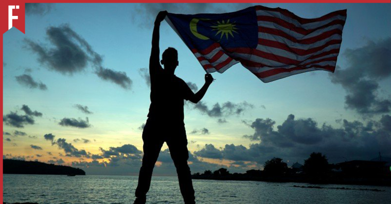 man raising jalur gemilang to celebrate malaysia day