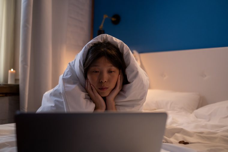 asian watching video on laptop in bed
